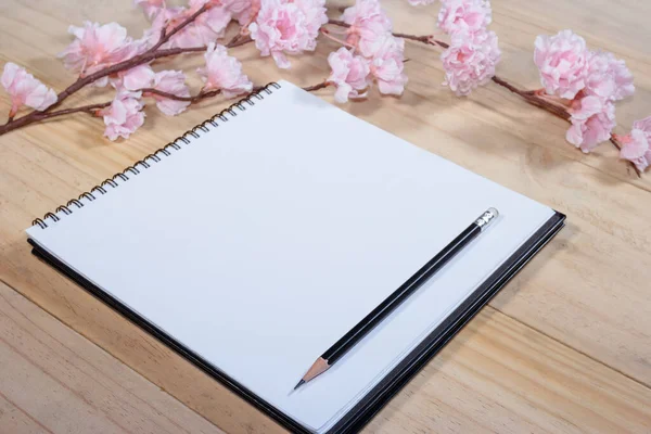 open note book with pink sakura flowers on wooden background
