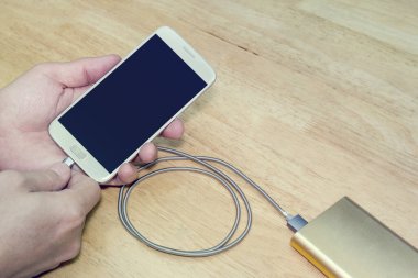 Akıllı telefon ahşap arka planda güç bankasıyla şarj ediliyor, filtre efekti