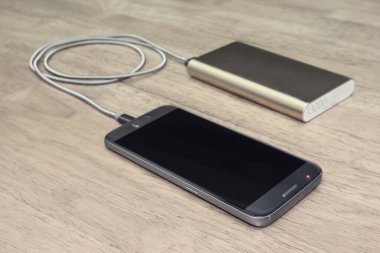 Tahta arka planda güç bankasıyla çalışan akıllı telefon, filtre efekti