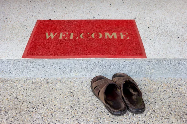 red welcome doormat on staircase and old sandals