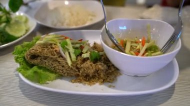 Mango salatasıyla çıtır yayın balığı yiyen kişi, Tayland yemeği.