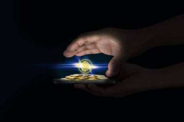 Siyah arka planda altın para yığınları ve bitcoin sembolü olan cep telefonu insan eliyle tutulur.