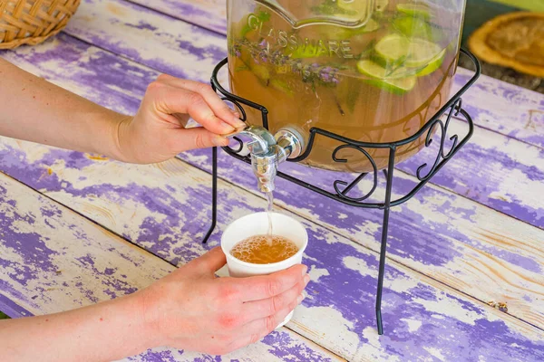 Homemade lemonade in vintage glass jar with lemons and limes on a wooden table, girl fills a glass