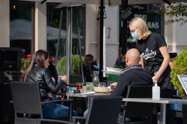 Sarışın, hoş, maskeli garson Covid ya da Coronavirus 'un ikinci dalgası sırasında açık hava barında, kafede ya da restoranda servis yapıyor. 