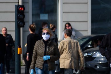 Maskeli ve eldivenli bir kadın şehir merkezinde kırmızı ışıkta yürüyor. Covid ya da Coronavirus salgını sırasında maskeler zorunlu, mecburi, ikinci dalga.