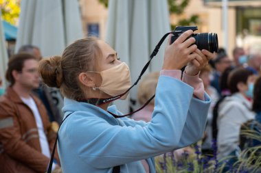 Covid veya Coronavirus salgını sırasında kamerayla fotoğraf çeken maskeli güzel kız halka açık bir etkinlikte, müzik festivalinde,