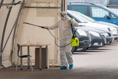 Koronavirüs veya COVID19 salgını sırasında araçlar için mobil test istasyonu çadırı dezenfekte eden koruyucu ekipman giyen sağlık görevlileri