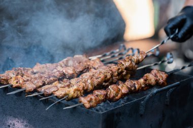 Izgarada siyah eldiven giymiş, domuz eti şişleri pişirirken çekilmiş yakın plan bir fotoğraf.