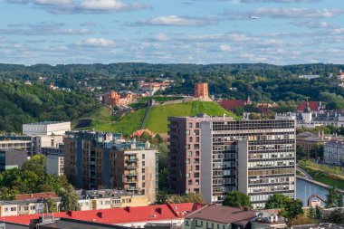 Vilnius şehri, Litvanya 'nın Gediminas Kalesi Kulesi ile çevrili yeşil bir tepe üzerinde yerleşim yerleri, ağaçlar, Neris nehri ve bulutlu mavi gökyüzü.