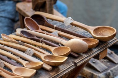 Geleneksel bir zanaat pazarında ahşap bir masa üzerinde çeşitli şekil ve boyutlarda el yapımı ahşap kaşıkların kırsal bir görüntüsü.