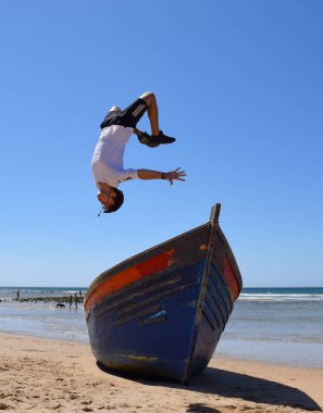 Bir çocuğun teknenin üzerinde uçarken ters takla atması. İspanya, Zahora plajında hile yapmak.