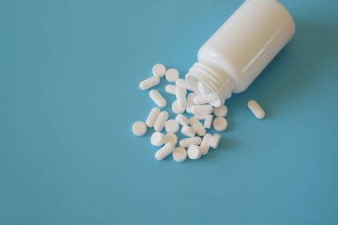Mavi arka planda plastik ilaç şişesinden çıkan tıbbi haplar. Parasetamol 500 mg, ilaç ve sağlık hizmeti konsepti. Üst görünüm.