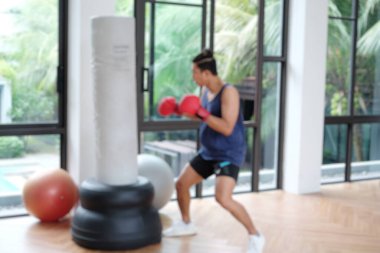 Asyalı bir sporcunun kırmızı boks eldiveni giyip spor salonunda kum torbasını yumruklarken bulanık bir fotoğrafı..