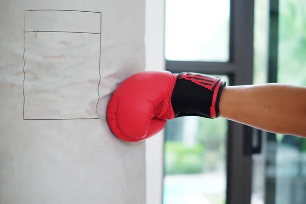 Close up hand with asian sport man wearing red boxing gloves punching heavy bag at training fitness gym.