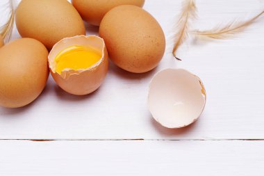 Tavuk tüyüyle kahverengi yumurta. Beyaz ahşap arka planda yumurta sarısı olan yumurta kabuğu. Boşluğu kopyala