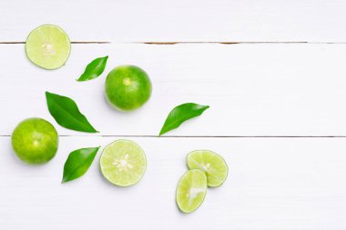 Düz, taze kireç, kepekli kireç dilimleri, beyaz ahşap masa zemininde yeşil yaprak. en üstteki görünüm.