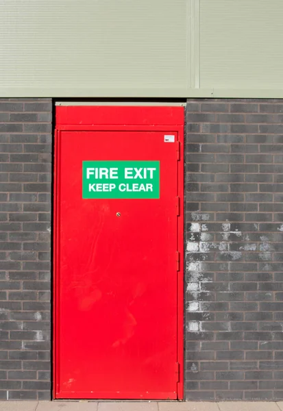 Kırmızı yangın çıkışı kapısı ve duvarda bir tabela.