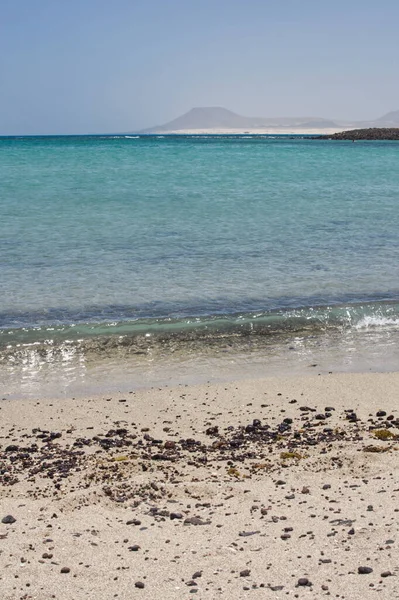 Sahildeki taşlar Lobos Adası Corralejo, Fuerteventura 'da kırılıyor. Dalgalar çakıl taşlarıyla kumlu bir sahile vuruyor.