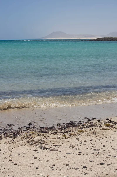 Sahildeki taşlar Lobos Adası Corralejo, Fuerteventura 'da kırılıyor. Dalgalar çakıl taşlarıyla kumlu bir sahile vuruyor.