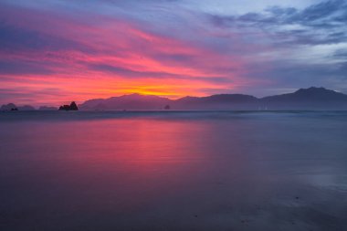 Sahilde gün batımı kırmızı-turuncu gökyüzü ıslak kumlara yansıyor. Banyuwangi, Endonezya 'da gün batımının manzarası