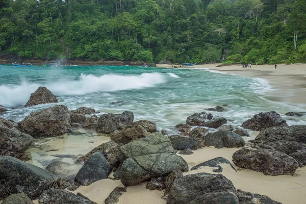 Yeşil su ve büyük dalgalı kayalık sahilin manzarası. Banyuwangi, Endonezya 'da ormanla çevrili beyaz kumlar.
