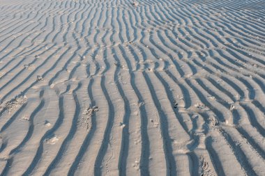 Endonezya 'daki Belitung Adası plajındaki dalgaların oluşturduğu kum üzerinde düşük açılı çizgi deseni. Belitung, Endonezya 'nın en popüler turizm merkezlerinden biridir..