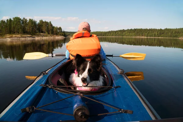 Der Besitzer und der Hund in einer Schwimmweste, die in einem Kajakboot schwimmt. — Stockfoto