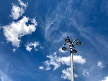 Beyaz bulutların ve mavi gökyüzünün arka planında bir sokak lambasının görüntüsü