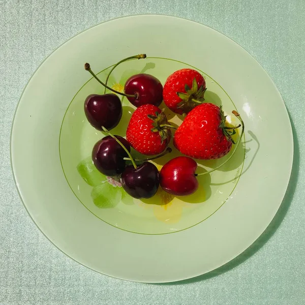 Cherries and strawberries over a green plate and on a light green background