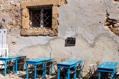 Mavi masalı, sandalyeli ve menüde Arancino al Rag yazan bir Sicilya restoranı. Menü tahtası duvara çivilenmiş.