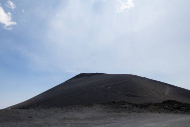 Etna Dağı 'ndaki lav tepesi ve volkanik kül. Mars ve gerçek dışı kayalar, kum ve siyah çakıl taşlarıyla iki turist tepenin zirvesinde yürüyüş yapıyor.