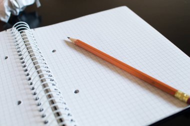 Kare ve turuncu kalemli bir not defteri. Sol üstte buruşuk bir çarşaf