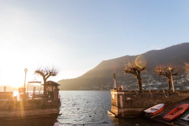Como Gölü 'ndeki küçük bir limanda balıkçı tekneleri depolanmış ve göl üzerinde toplu taşıma için feribot döşenmiş. Günbatımında ışıklar Como Gölü 'ndeki Torno köyünden geliyor.