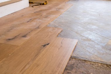 Açık bir pencerenin yakınındaki eski bir taş eşya katındaki kurulum sırasında meşe rengi parke. Sabahleyin bir apartman dairesinin tadilatı sırasında çimenlik ışık.