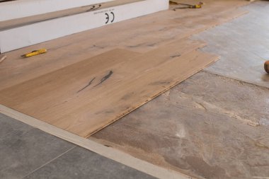 Açık bir pencerenin yakınındaki eski bir taş eşya katındaki kurulum sırasında meşe rengi parke. Sabahleyin bir apartman dairesinin tadilatı sırasında çimenlik ışık.