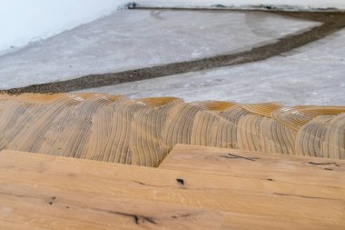 Açık bir pencerenin yakınındaki eski bir taş eşya katındaki kurulum sırasında meşe rengi parke. Sabahleyin bir apartman dairesinin tadilatı sırasında çimenlik ışık.