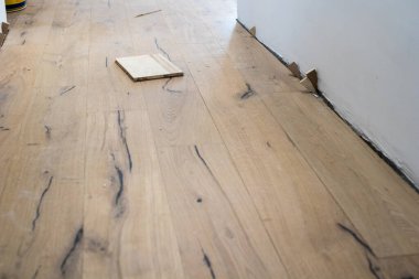 Bir dairenin yenilenmesi sırasında parke tahtalarının kurulması, yeni monte edilmiş beyaz bir duvarın yanındaki meşe ağacından bir tahta parçası.