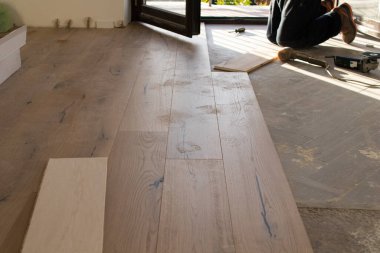 Açık bir pencerenin yakınındaki eski bir taş eşya katındaki kurulum sırasında meşe rengi parke. Sabahleyin bir apartman dairesinin tadilatı sırasında çimenlik ışık.