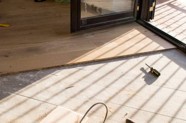 Açık bir pencerenin yakınındaki eski bir taş eşya katındaki kurulum sırasında meşe rengi parke. Sabahleyin bir apartman dairesinin tadilatı sırasında çimenlik ışık.