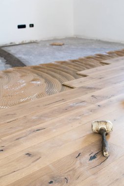 Açık bir pencerenin yakınındaki eski bir taş eşya katındaki kurulum sırasında meşe rengi parke. Sabahleyin bir apartman dairesinin tadilatı sırasında çimenlik ışık.