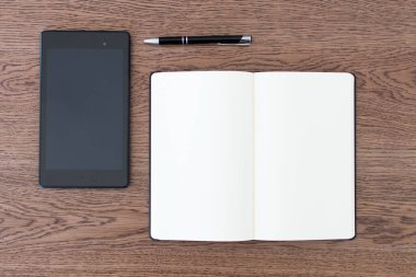 Defter, tablet ve kalem ahşap bir masaya. Gazeteci ya da blog yazarı için çalışma alanı. Sosyal medya ve defter üzerinden internet üzerinden gazetecilik faaliyetleri. Analog ve dijital birlikte