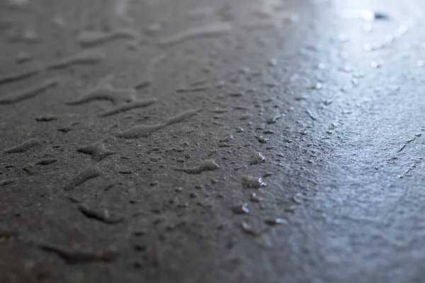 Raw and rough black granite slab wet with water. Drops and patches of water on a slab of black granite, freshness and elegance in furnishing and building supplies. Black stone with drops of water