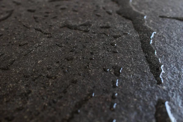 Raw and rough black granite slab wet with water. Drops and patches of water on a slab of black granite, freshness and elegance in furnishing and building supplies. Black stone with drops of water