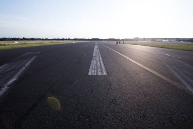 Orta şeritte beyaz şeritli asfalt yol. Ovadaki uzun düz asfalt yola bakış açısı çatlaklar ve eskimiş beyaz boya, gün batımında güneş ışığı arka planda..