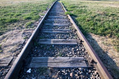 Çimen ve ahşap yataklı kullanılmayan bir demiryolunun rayları. Bakış açısına göre eski demiryolu hattı, ufuktaki demir raylar gibi birleşiyor