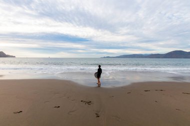 Suya girmeye hazır sörfçü güçlü ve yüksek bir dalga bekliyor. Sörf ve su sporlarını özgürce yapabileceğiniz bir sahilde kış günü.