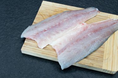fillet of filleted sea bass on a wooden table and a slab of black granite. Fresh sea fish ready to be cooked. Two halves of sea bass fillet without bone clipart
