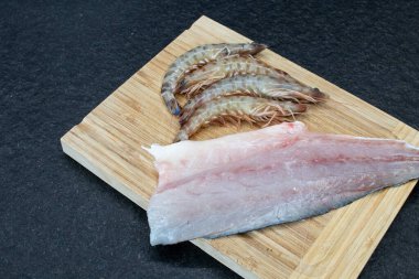 Tahta kesme tahtasında karides ve siyah granit bir masa olan ringa kemiği olmayan deniz kabuğu filetosu. Taze ve çiğ balık yenmeye hazır. Balık ve kabuklu taze ve sağlıklı yiyecekler.