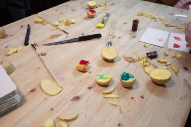 Patates doğrama. Patates, renkli mürekkep, bıçaklar ve kağıt. Patatesle pul yapmak için. Çocuklar için eğitici bir aktivite. Patates oyarak bir pul yaratıyorlar.