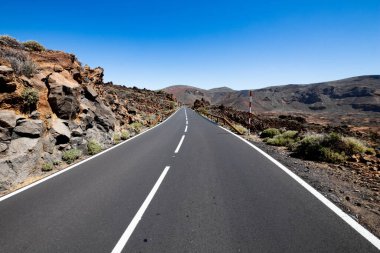 Taşları ve boş tabelaları olan ıssız bir yol. Ufuk olarak mavi gökyüzü ve asfalt bir yol perspektifinde düz
